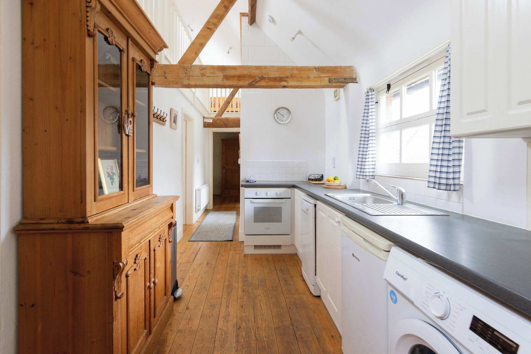 A kitchen with wooden cabinets, a washing machine, a dishwasher, and a window with checkered curtains.