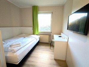Una habitación pequeña con una cama, un escritorio y un televisor.