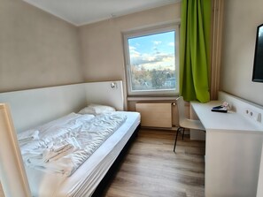 Una habitación con cama, escritorio, ventana con vistas y radiador.