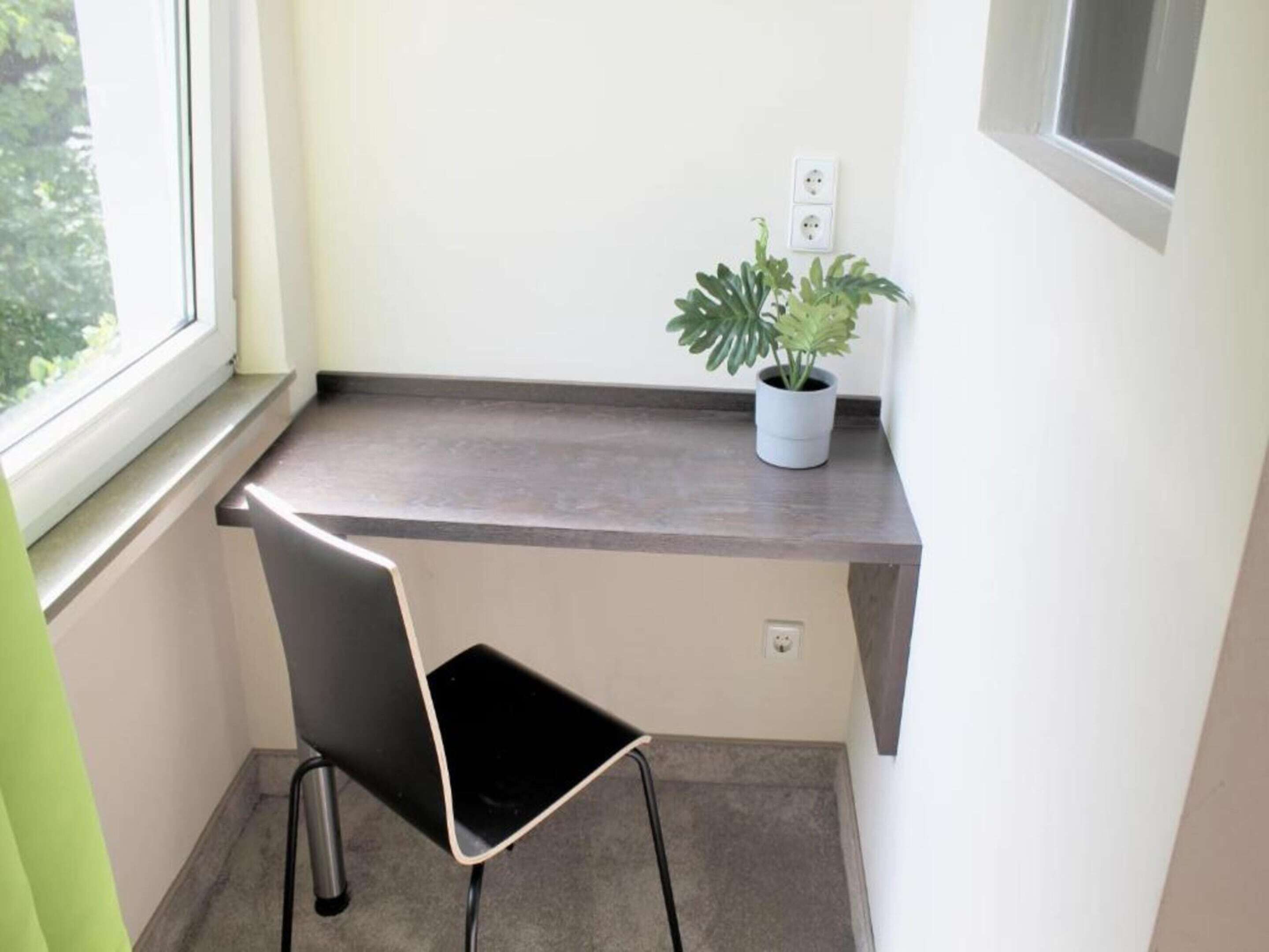 Een kleine werkruimte met een bureau, stoel, potplant en een raam.