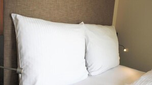 Een net opgemaakt bed met witte lakens en kussens, een hoofdbord en een bedlampje.