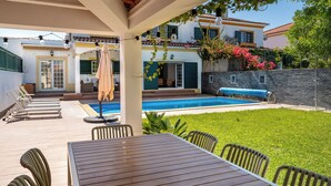 Un espacio al aire libre techado con piscina, sillas de descanso y una mesa.