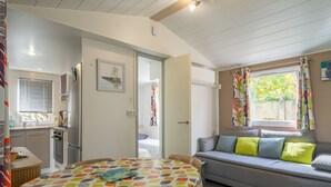 Habitació amb llit, sofà, taula de dinar, zona de cuina i finestra amb cortines.
