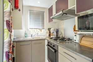 A compact kitchen with a gas stove, oven, and a microwave. - Mobile Home near Royan-Oléron with Shared Pool, Private Terrace & Air Conditioning (Saint-Sornin)