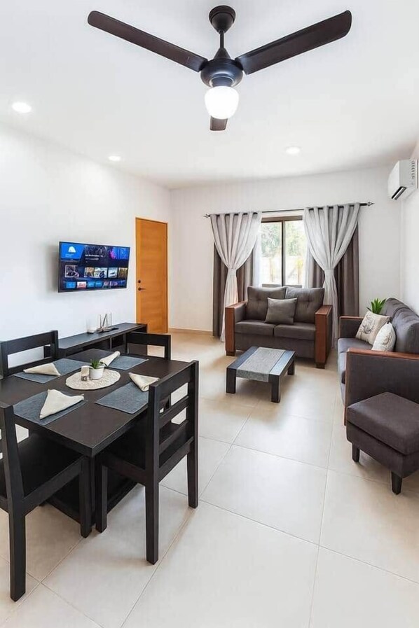 Una sala de estar moderna con una mesa de comedor, sofás, un televisor y un ventilador de techo.