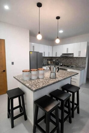 Eine moderne Küche mit weißen Schränken, einer Granit Arbeitsplatte und vier schwarzen Barhocker.