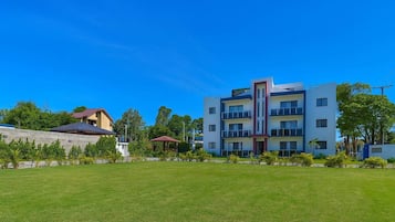 Un immeuble moderne à plusieurs étages, doté de balcons, d’une pelouse bien entretenue et entouré de verdure.