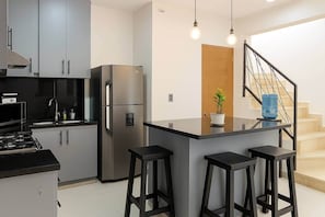 Cozinha moderna com ilha central, banquetas, geladeira e escada.
