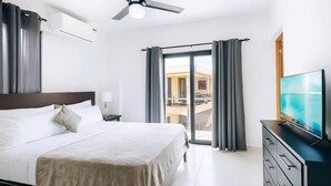 Ett hotellrum med en säng, en TV, en byrå och en balkong med gardiner.