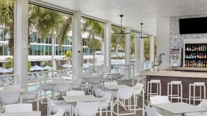 A modern outdoor seating area with white tables and chairs, large windows, and a bar with a stone wall. - Amazing 2 Bedroom Marco Island, FL Marriott - Crystal Shores Resort (Marco Island)