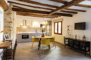 Una cocina con electrodomésticos modernos, una mesa de comedor con sillas, una pared de piedra y un televisor montado en la pared.