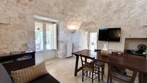 Une pièce aux murs de pierre, comprenant une table à manger, des chaises, un téléviseur fixé au mur et un radiateur.