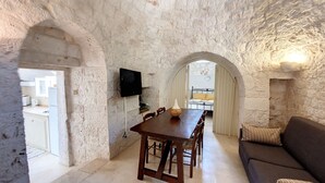 Une pièce aux murs de pierre, comprenant une table à manger, des chaises, un canapé et un téléviseur fixé au mur.