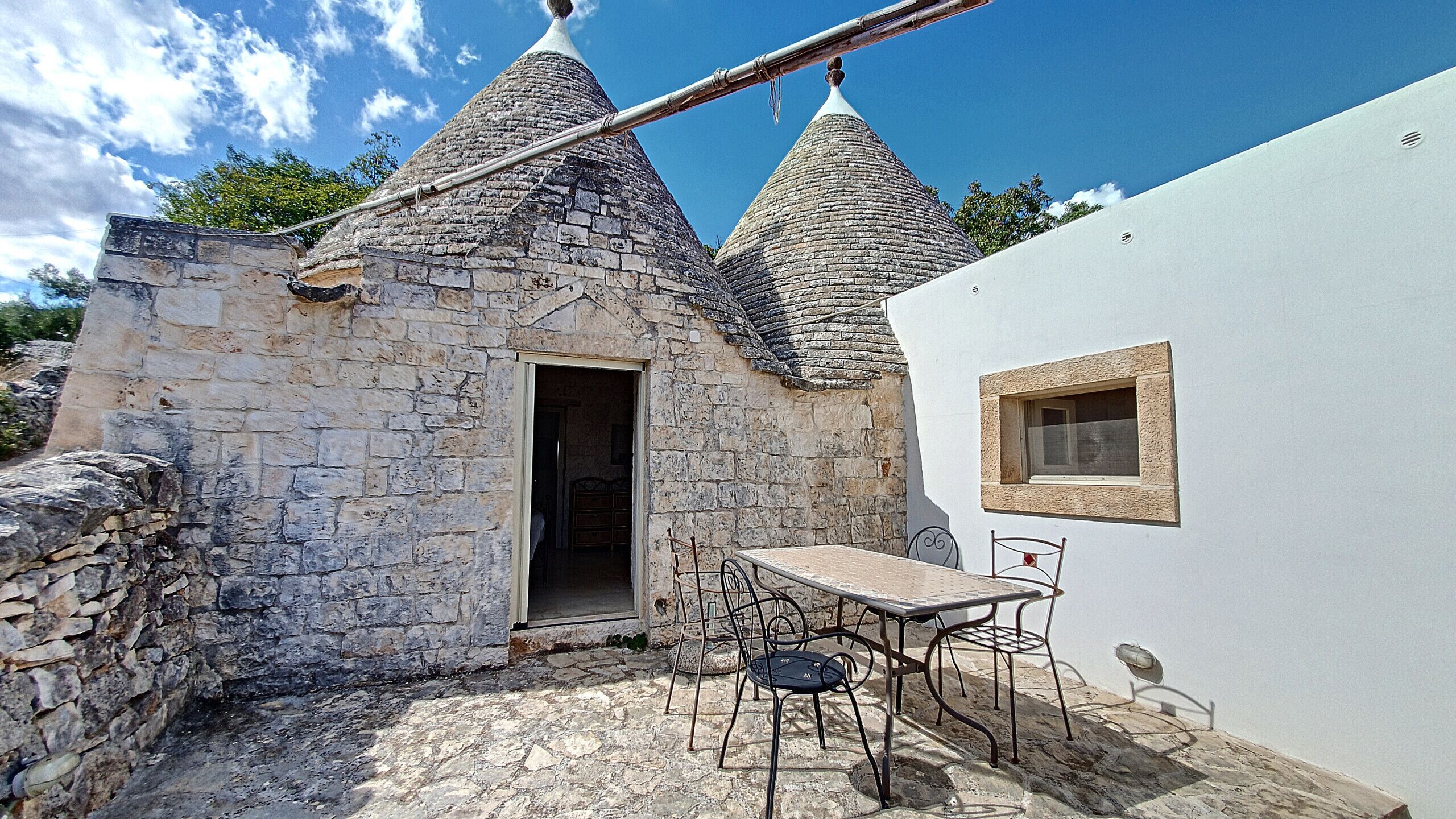 A stone building with a small door, a table with chairs, and a window.