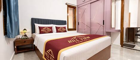 Una habitación de hotel con una cama grande, una mesita de noche, una lámpara, un armario y una ventana con persianas.
