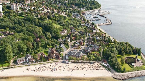Egy tengerparti város légi felvételén lakóövezetek, egy jachtkikötő és egy homokos strand látható.