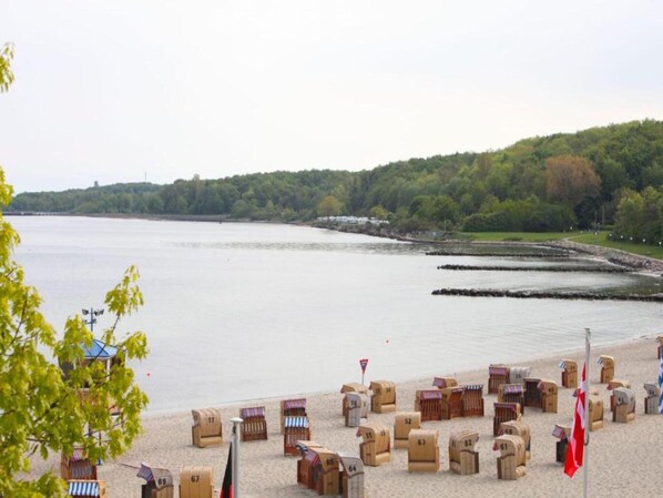 A beach with wooden structures, a lifeguard tower, and a forested hill in the background.