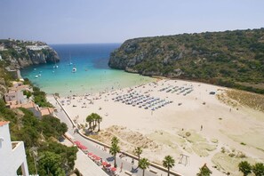 A coastal beach with a paved walkway, beach umbrellas, and a clear view of the sea. - Villa Marques by Villa Plus (Cala en Porter)