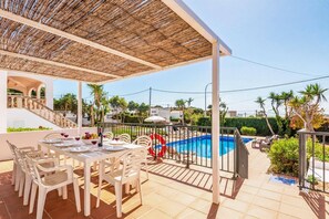 Un área de comedor al aire libre techada con piscina y sillas de descanso.