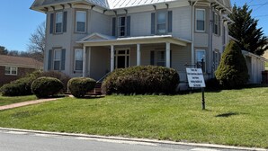 A two-story house with a covered porch, a chimney, and a sign indicating it is a guest house. - Perfect for Everyone - 8-bedrooms - The Future Generations University Guesthouse (Franklin)