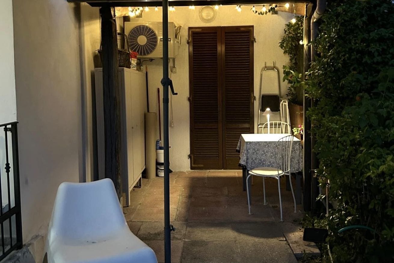 A covered outdoor patio with a table and chairs, a white plastic chair, and a closed door.