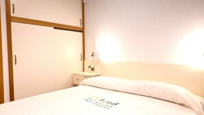 Hotellihuone, jossa on sänky, yöpöytä, lamppu ja vaatekaappi.