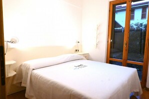 A small, well-lit bedroom with a single bed, a nightstand, a lamp, and a sliding glass door to the outside. - M453 - Marcelli, comfortable two-room apartment with garden (Marcelli)