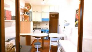 Pieni, käytännöllinen keittiö, jossa on valkoiset kaapit, pieni ruokapöytä ja yksi tuoli.