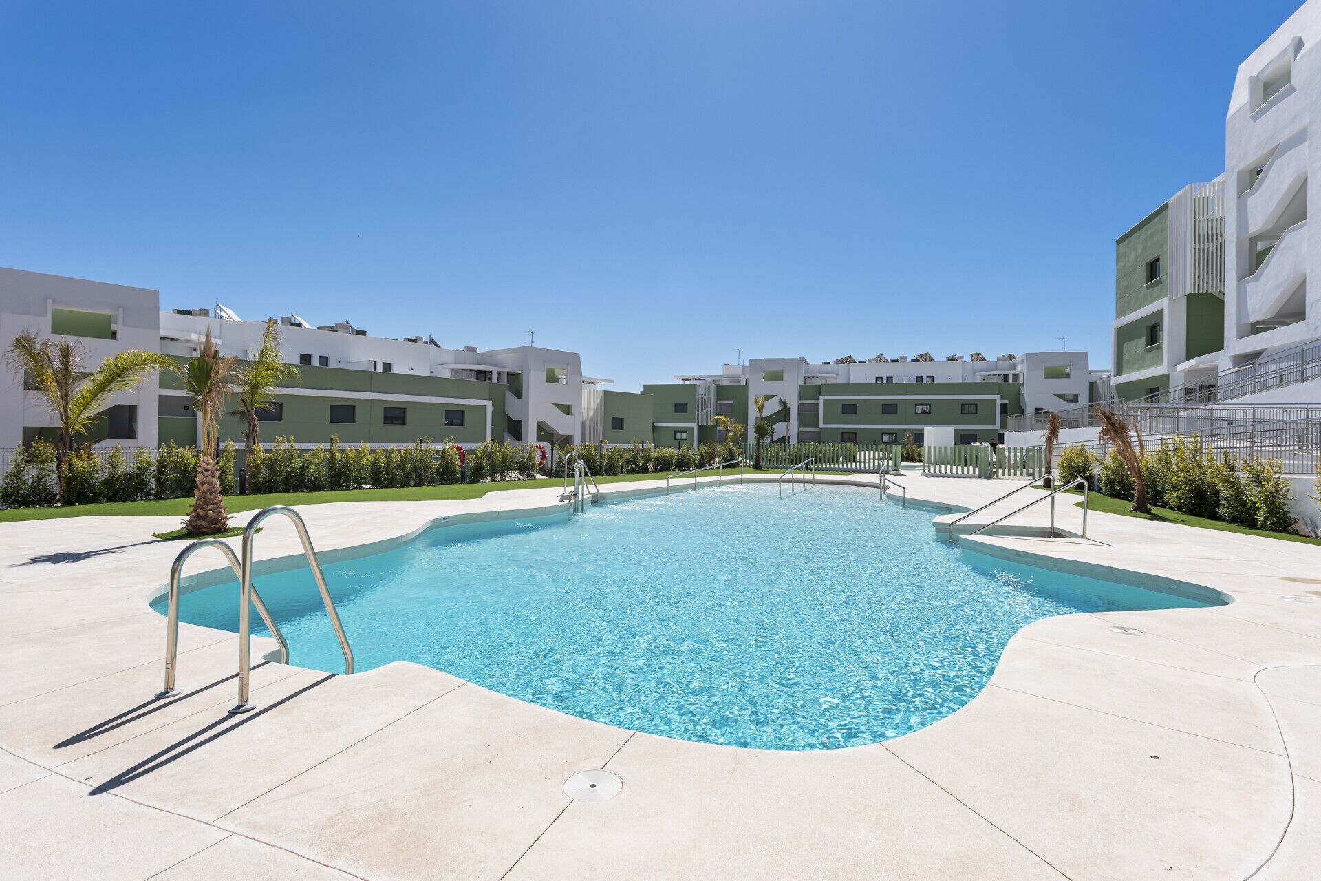 A swimming pool with a clear blue water, surrounded by a paved area, and modern buildings in the background.
