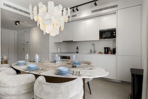 A modern kitchen with white cabinets, a Bosch microwave, and a dining area with a marble table and white chairs. - Golfside 3BR Apt with large Terrace, Pool & Spa (Mijas)