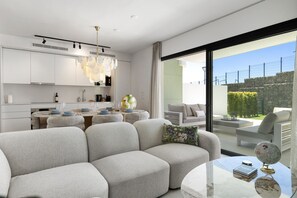 A modern kitchen with white cabinets, a dining area with a round table, and a living area with a sofa and a glass coffee table. - Golfside 3BR Apt with large Terrace, Pool & Spa (Mijas)