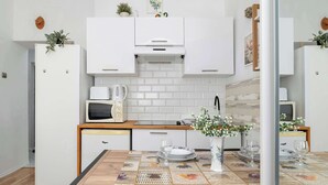 A modern kitchen with white cabinets, a microwave, a kettle, and a dining table set with plates and glasses. - Functional Studio | Air Conditioning | Space to work (Kraków)