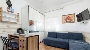 A modern living room with a sofa, a desk with a chair, a TV, and a large mirror. - Functional Studio | Air Conditioning | Space to work (Kraków)