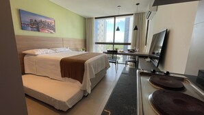 Habitación de hotel con cama, escritorio, televisor y ventana con vista a la ciudad.