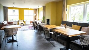 Una sala de estar moderna con un sofá, una mesa de comedor y sillas. Hay ventanas amplias con cortinas, una chimenea y un televisor.