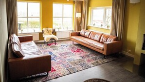 A living room with a brown leather sofa, a patterned rug, and a chair. - Hotel de Horper Wielen (Kaard)