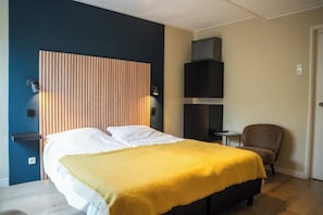 Un dormitorio con cama, mesitas de noche, una silla y un televisor instalado en la pared.