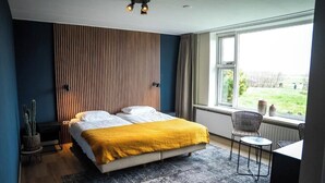 Un dormitorio con cama, ventana, silla y una mesita.