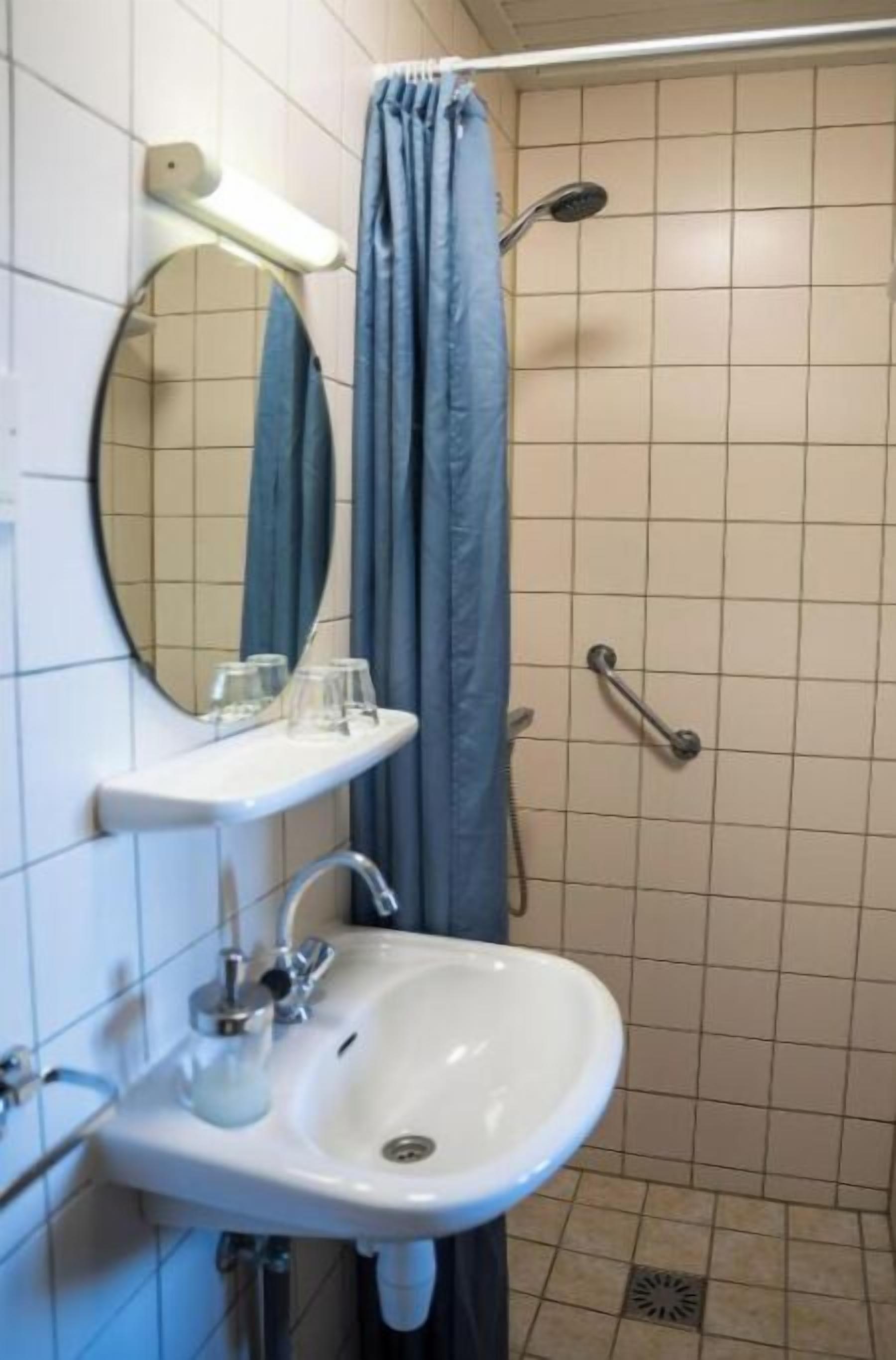 Un baño con lavamanos blanco, espejo y ducha con cortina.