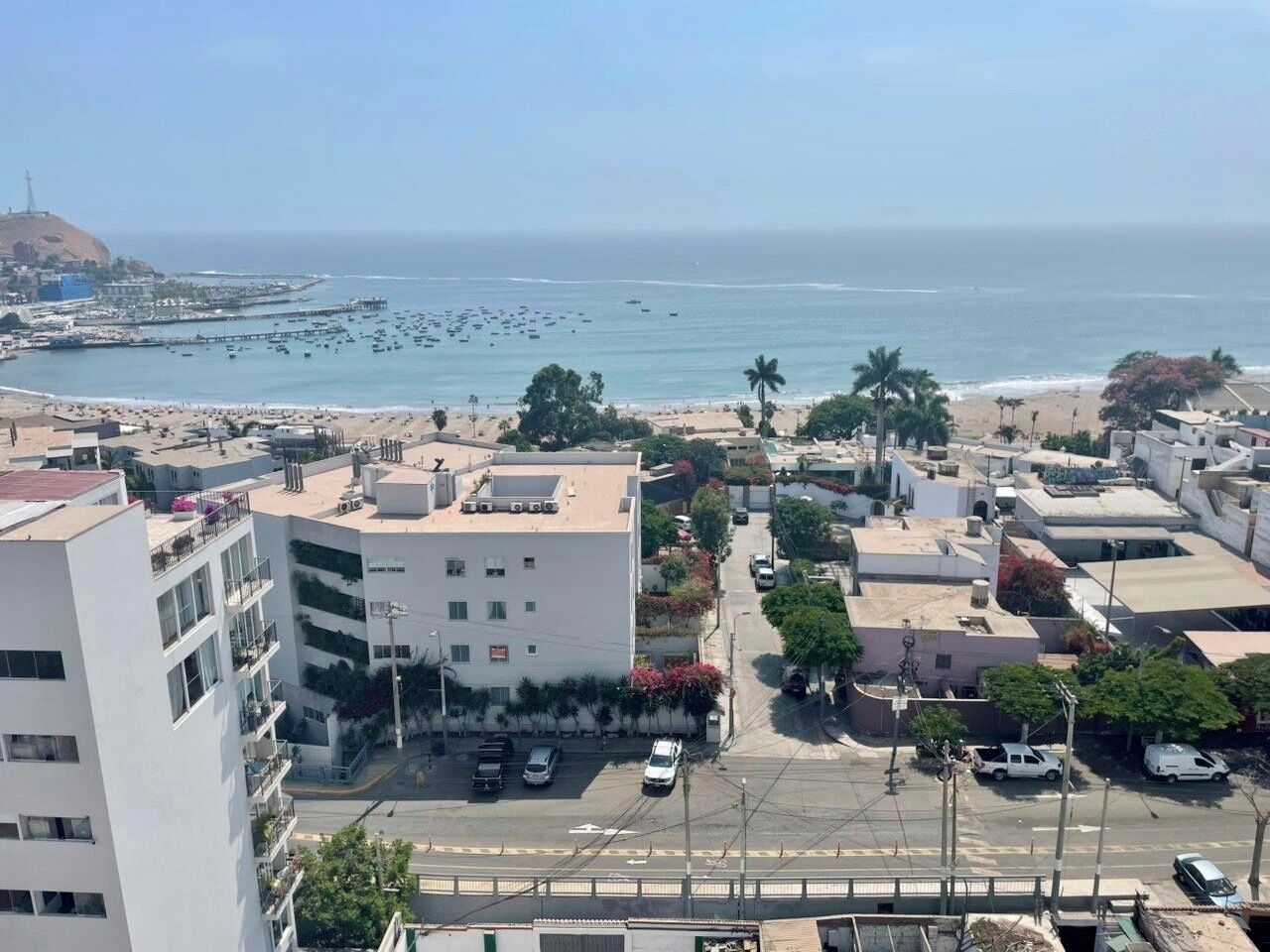 A coastal cityscape with a prominent white building, a beach, and a clear view of the ocean.
