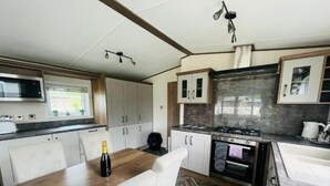 A modern kitchen with a wooden table, white chairs, a microwave, cabinets, a stove, and a sink.