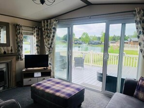 A room with a bed, a TV on a stand, a fireplace, and large sliding glass doors to a deck. - Lakeside Escape Lodge with Hot tub (york)