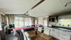 A compact RV interior with a dining area, kitchenette, and a large window offering a view of a residential area.