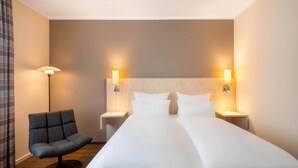 Una habitación de hotel con cama, dos mesitas de noche, una silla y lámparas de pared.