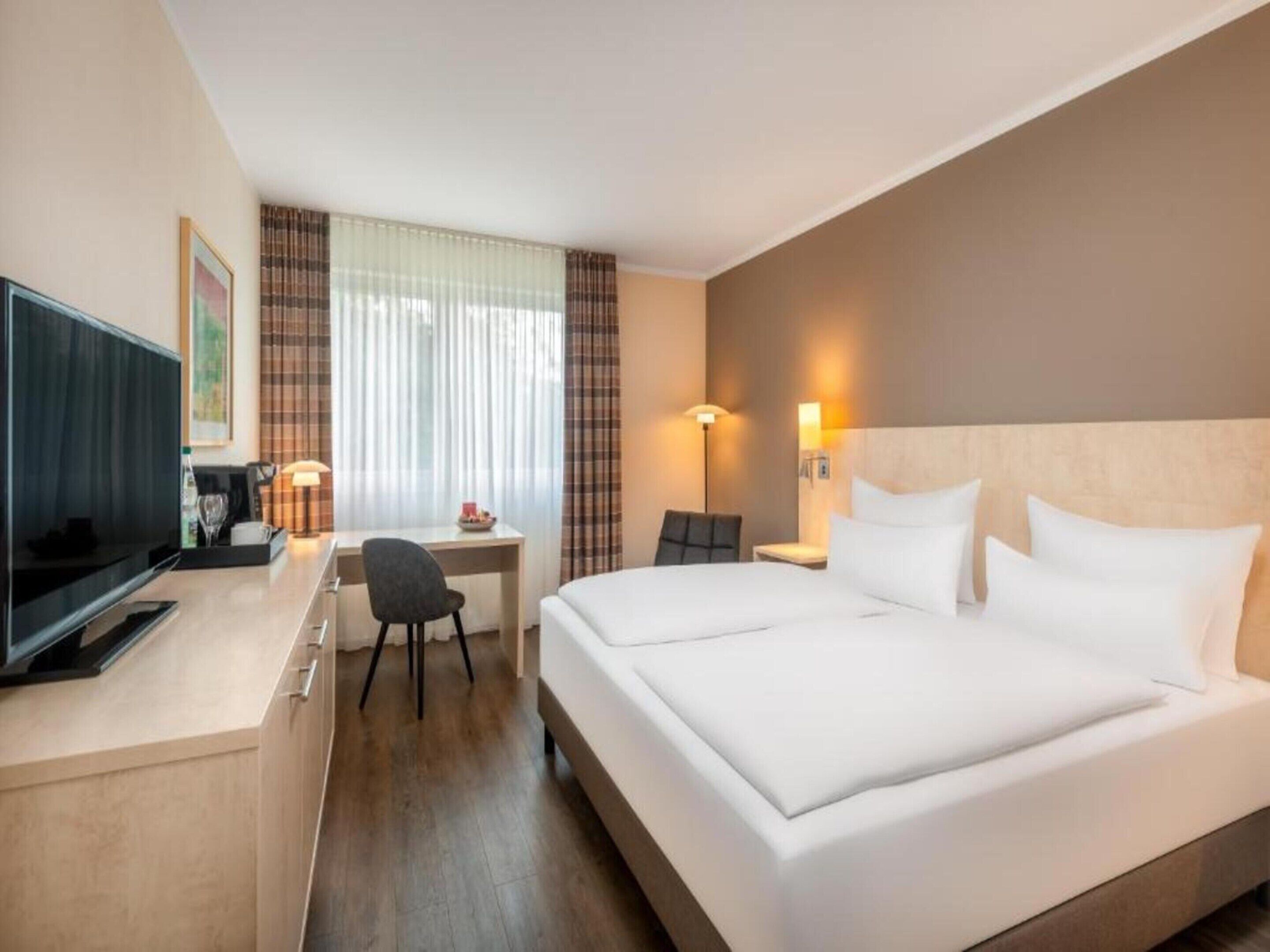 A hotel room with a bed, desk, chair, television, and a window with curtains.