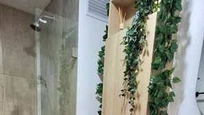 A bathroom with a glass-enclosed shower, a toilet, a sink with a wooden cabinet, and a mirror with a plant decoration. - U-GO Torre Evoca Centro de la Ciudad (Bogotá)