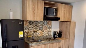 A kitchen with a black refrigerator, wooden cabinets, a microwave, and a tiled backsplash. - U-GO Torre Evoca Centro de la Ciudad (Bogotá)