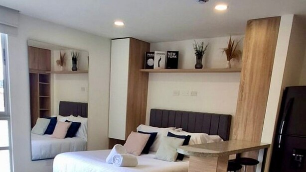 A modern bedroom with a bed, a built-in wardrobe, a small seating area, and a kitchen counter. - U-GO Torre Evoca Centro de la Ciudad (Bogotá)