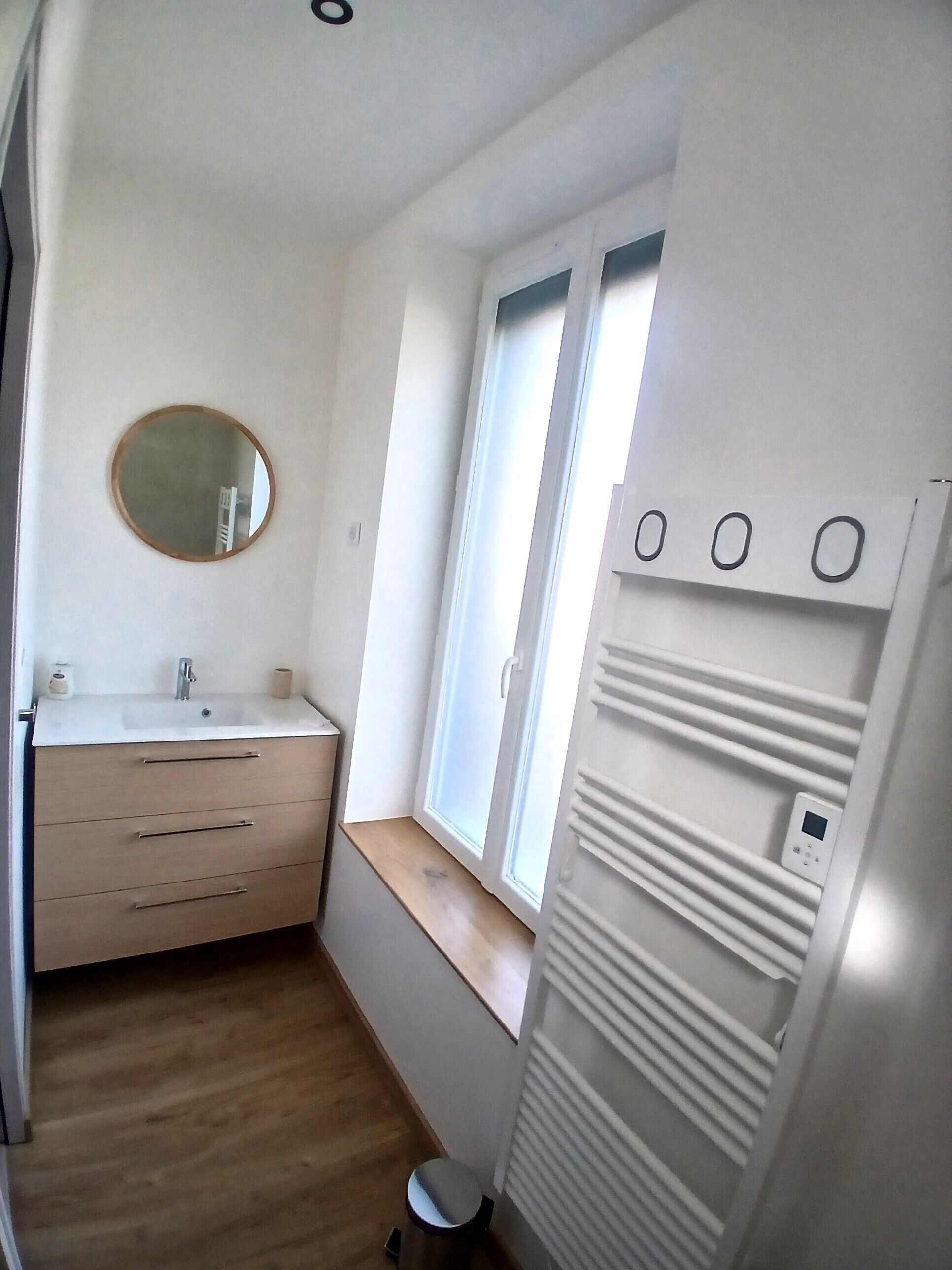 A small, modern bathroom with a white sink, mirror, and window.