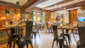 A rustic interior with exposed wooden beams, stone walls, and a bar area with stools and glasses.